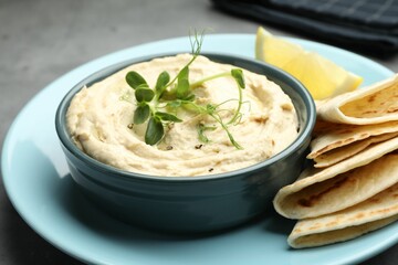 Delicious hummus in bowl, pita and lemon on table, closeup