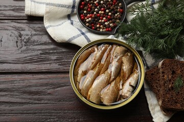Tasty sprats in tin can, peppercorns, bread and dill on wooden table, top view. Space for text