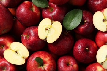 Fresh ripe red apples and green leaves as background, top view