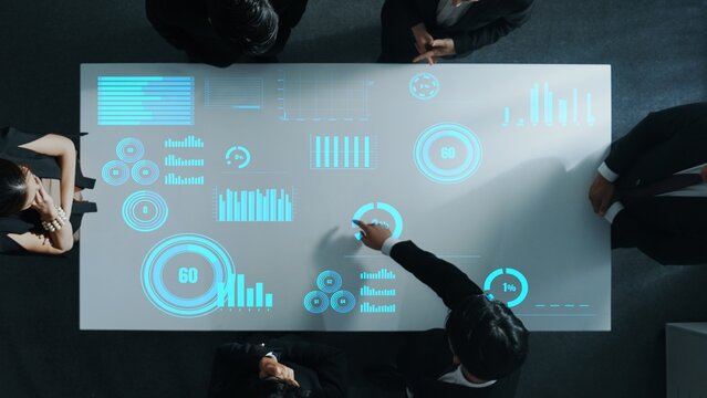 Top down aerial of collaborate professional diverse business people discuss marketing strategy with hologram of marketing data analysis graph, diagram or financial profit investment plan. Directorate.