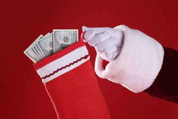 Santa holding stocking with dollar banknotes on red background, closeup