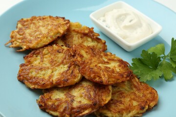 Delicious potato pancakes, sour cream and parsley on plate, closeup