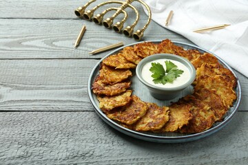 Delicious potato pancakes, menorah and candles on gray wooden table, closeup. Hanukkah festive food