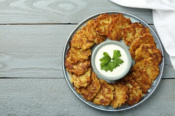 Delicious potato pancakes and sour cream on gray wooden table, top view. Space for text
