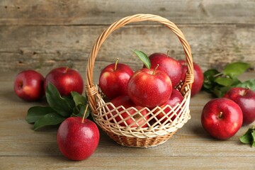 Fresh ripe red apples in wicker basket on wooden table