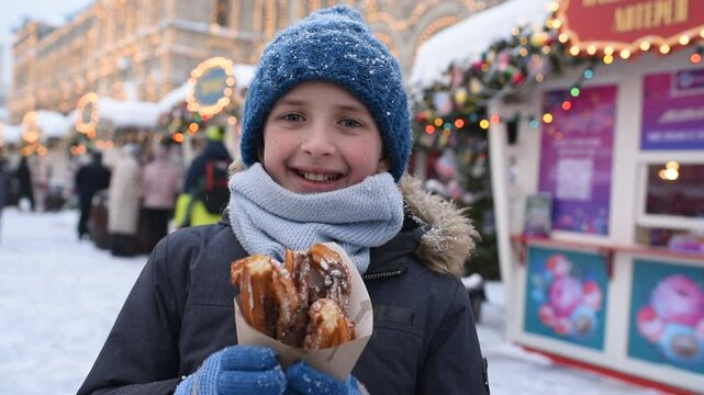 boy, child, schoolboy, tourist in winter clothes eats churros at the Christmas market on a snowy winter day.
