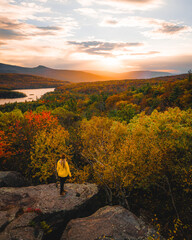 Beautiful Female Adventure Travel Hiker Yellow Coat Stands on Rock Wide View Sunset Rock Catskills New York New England Fall Foliage Autumn Season