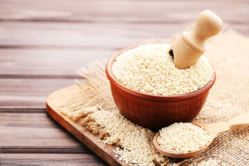 Sesame seeds in spoon and bowl with cutting board and sackcloth on wooden background