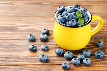 Blueberries with mint leafs in yellow mug on wooden background