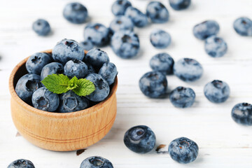 Sweet blueberries with green leaf in bowl on wooden background
