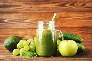 Green smoothie in glass jar with fruits and vegetables on brown wooden background