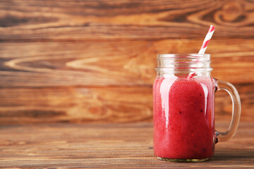 Red smoothie in glass jar on brown wooden background