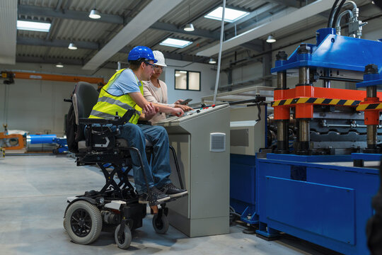 Female manager training a new employee with a disability for a job, explaining work on machines. Industry, inclusion and workplace concept.