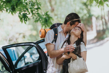 A joyful couple shares an affectionate embrace outdoors while holding their cat. The image captures...