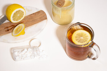 Hot tea with fresh lemon and honey, a bottle with white pills on white table
