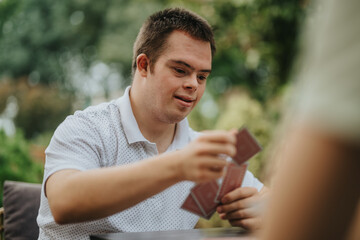 A young man with Down syndrome enjoying a card game outside in a relaxed setting, showcasing...