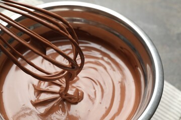 Chocolate dough dripping from whisk into bowl on table, closeup