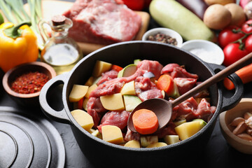 Cooking stew. Uncooked meat, vegetables and pot on black table