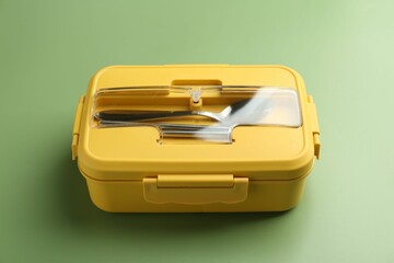 Yellow lunch box with cutlery on green background