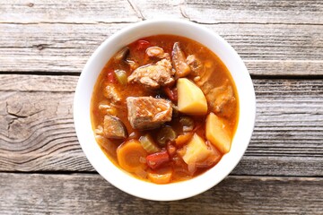 Delicious stew with vegetables in bowl on wooden table, top view