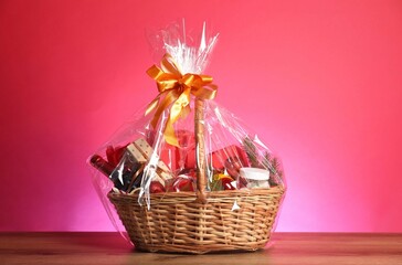 Wicker gift basket with wine on wooden table against pink background