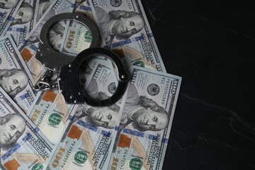 Corruption. Handcuffs and dollar banknotes on black table, top view. Space for text