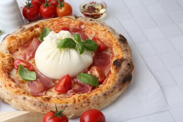 Delicious pizza with burrata cheese, basil, tomatoes and ham on white tiled table, closeup
