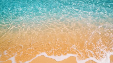 Obraz premium Top view of clear blue sea and bright, golden sand, with sunlight casting reflections on the water
