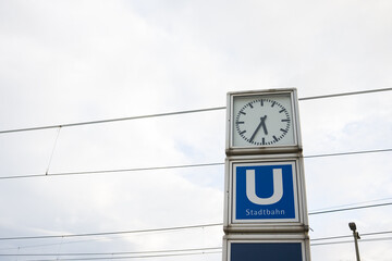 City clock at a public transport stop. Dial with clock outside in cloudy weather.