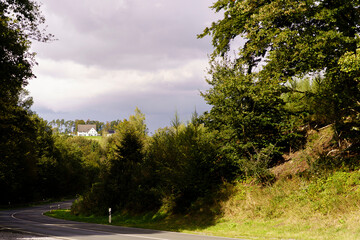 Landscape autumn photo of a small house in the distance behind the road and trees. Early autumn in Germany