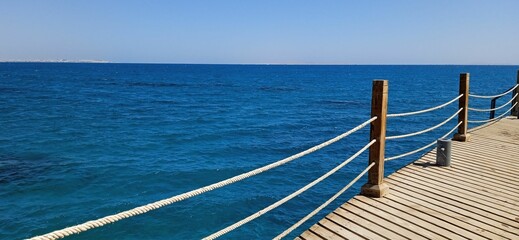 Obraz premium Wooden dock extending out into the blue ocean waters under a clear blue sky