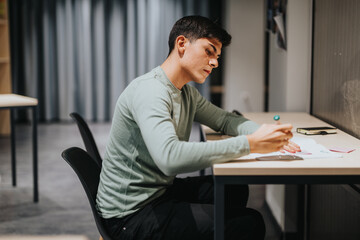 A focused high school student sitting at a desk during class, deeply engaged in studying with...