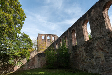 A stone wall with arched windows stands tall against a blue sky, remnants of a historic building in Germany