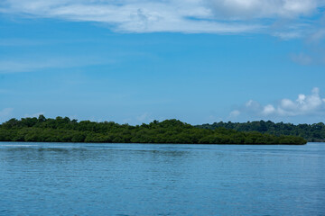 Beautiful island scenery with a bright blue sky, green foliage, and calm waters reflecting the natural beauty of the coastline, environment for travel, summer vacations, peaceful retreats