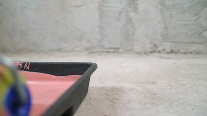 Construction worker painting a wall with pink paint using a roller.