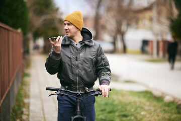 Naklejka premium Man Recording Voice Message While Leaning on a Bicycle