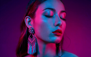 A close-up portrait of a woman against a vibrant purple background. She has her eyes closed, and her makeup is accentuated with shades of blue and pink.