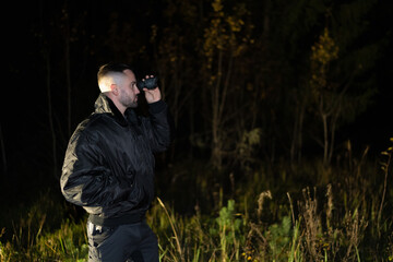Obraz premium A man with a night vision device in his hand in a dark forest at night.