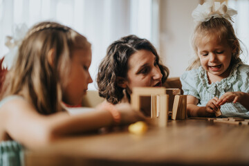 A joyful family moment with a mother and her daughters engaged in creative play using wooden blocks. They are sharing smiles and bonding indoors.