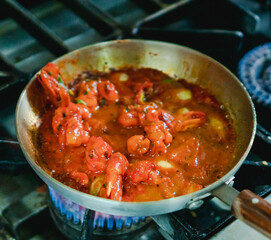 Mouthwatering flavorful shrimp dish. The shrimp are vividly red, surrounded by a glossy sauce with hints of spices. There are visible chunks of garlic and possibly other aromatics.