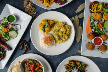 Dinner table decorated with mouthwatering Indian cuisine colorful plates with rice, spicy curries, crispy naan bread, and fresh salads adorned with herbs—garnishes of bright vegetables and chutneys.