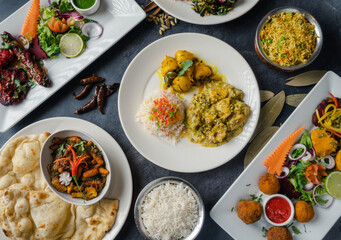 Dinner table decorated with mouthwatering Indian cuisine colorful plates with rice, spicy curries, crispy naan bread, and fresh salads adorned with herbs—garnishes of bright vegetables and chutneys.