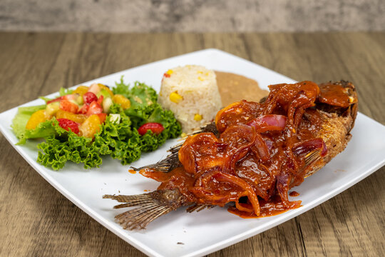 Grilled mojarra fish with spicy shirmp diablo dinner served with rice and beans on a wooden platter