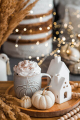 Delicious pumpkin latte with whipped cream and cinnamon in a mug on the table in the living room interior. Autumn decor in the house. Scandinavian style.