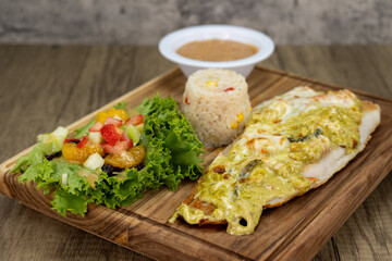 Grilled Basa fish fillet smothered in gratinado cheese dinner served with rice and beans on a wooden platter