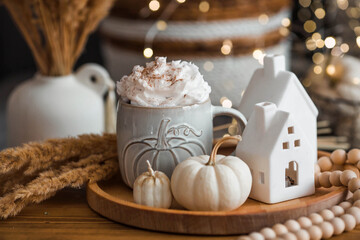 Delicious pumpkin latte with whipped cream and cinnamon in a mug on the table in the living room interior. Autumn decor in the house. Scandinavian style.