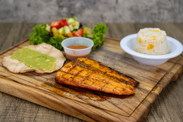 Grilled salmon dinner served with rice and gucamole on a wooden platter