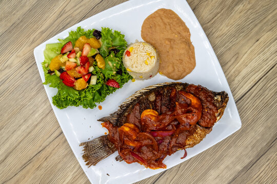 Overhead view of grilled mojarra fish with spicy shirmp diablo dinner served with rice and beans on a wooden platter