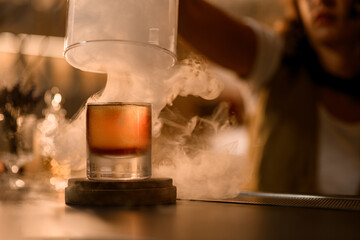 Glass with a brown drink stands on a wooden stand, around which steam spreads