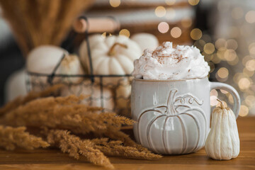 Delicious pumpkin latte with whipped cream and cinnamon in a mug on the table in the living room interior. Autumn decor in the house. Scandinavian style.